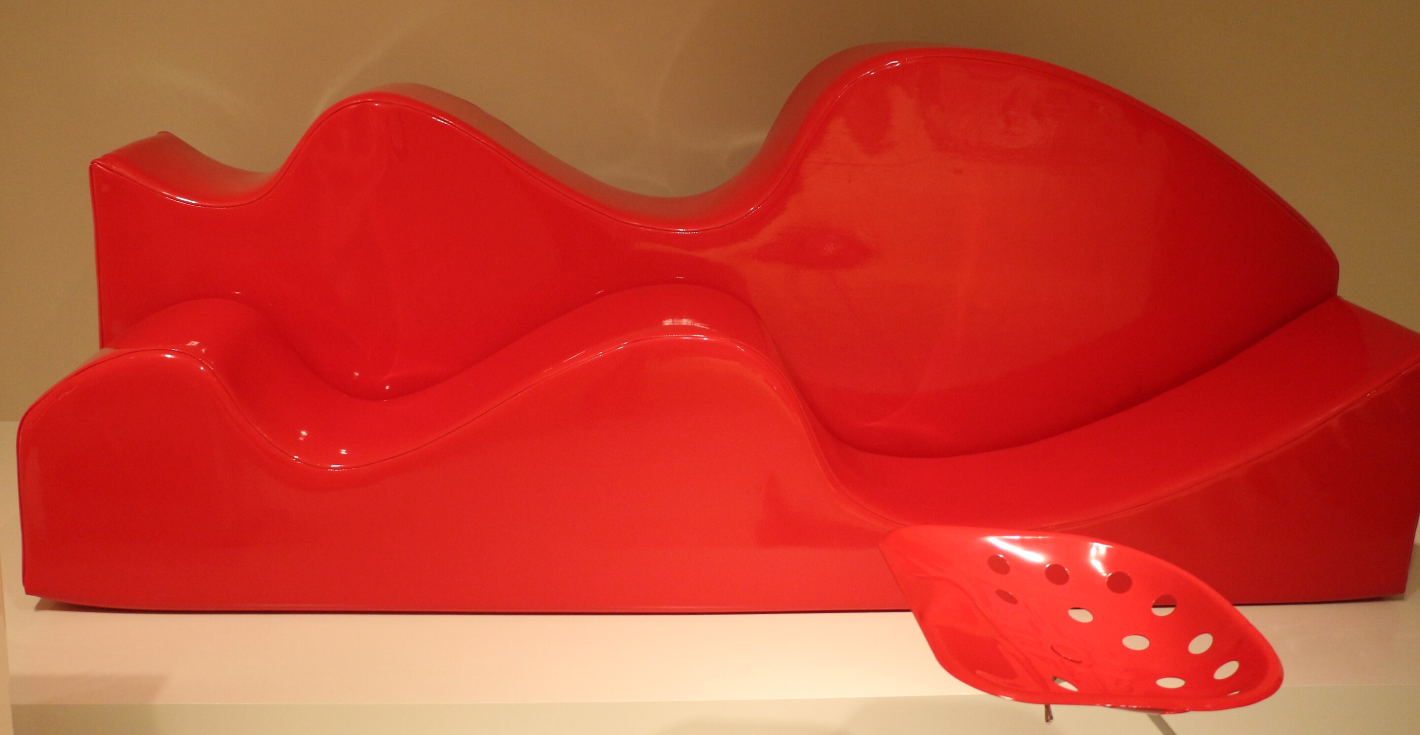 A wavy red plastic chair that critiques the shape of a sofa